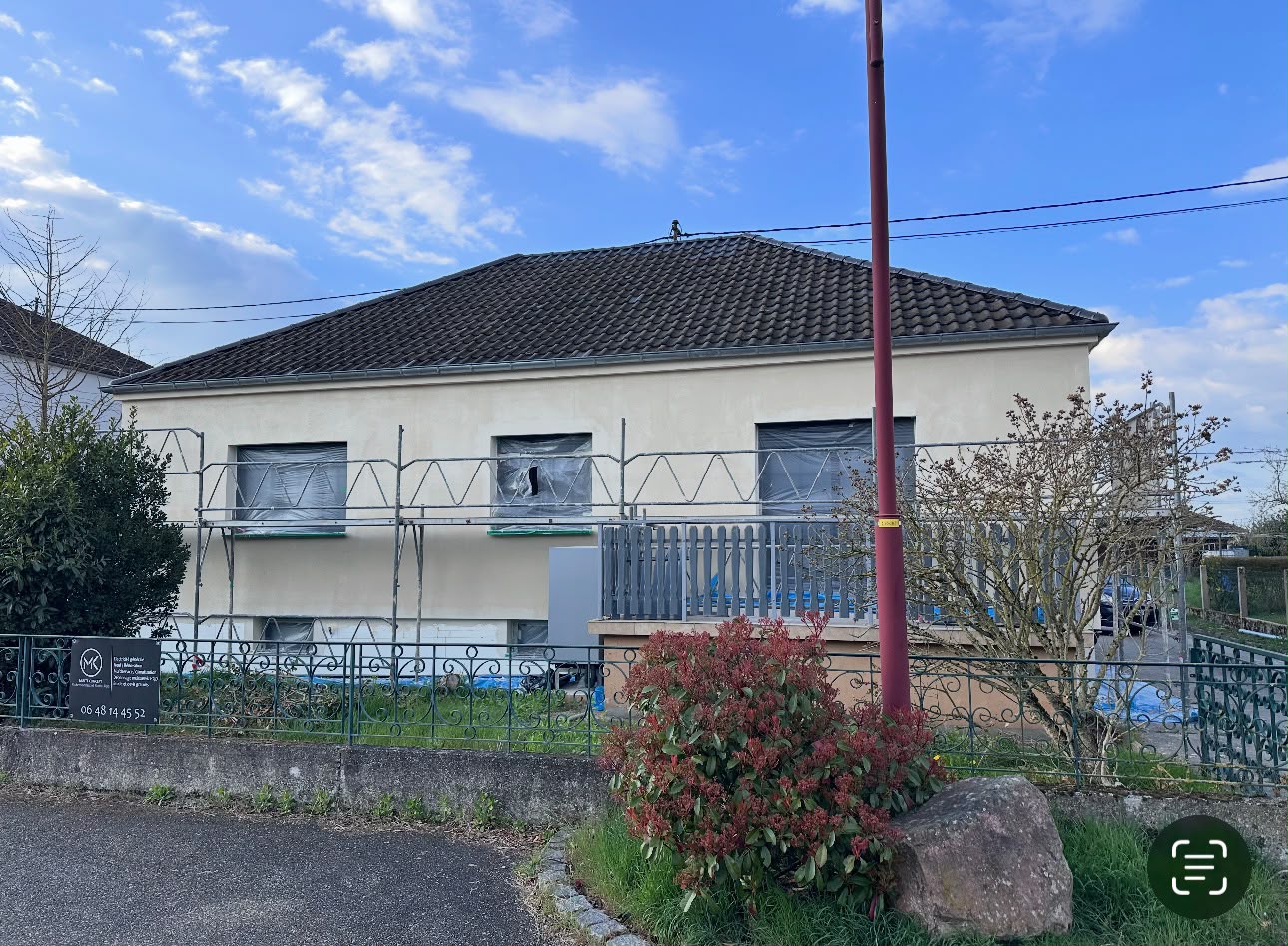 Façade beige de maison sous échafaudage, fenêtres protégées par un film, bâche au sol