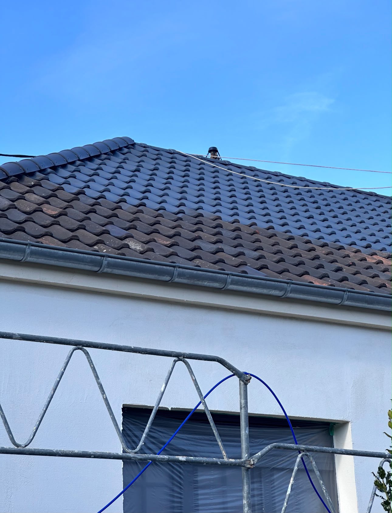 Toiture en cours de peinture, moitié grise, moitié brun-rouge, gouttière grise et façade blanche en dessous