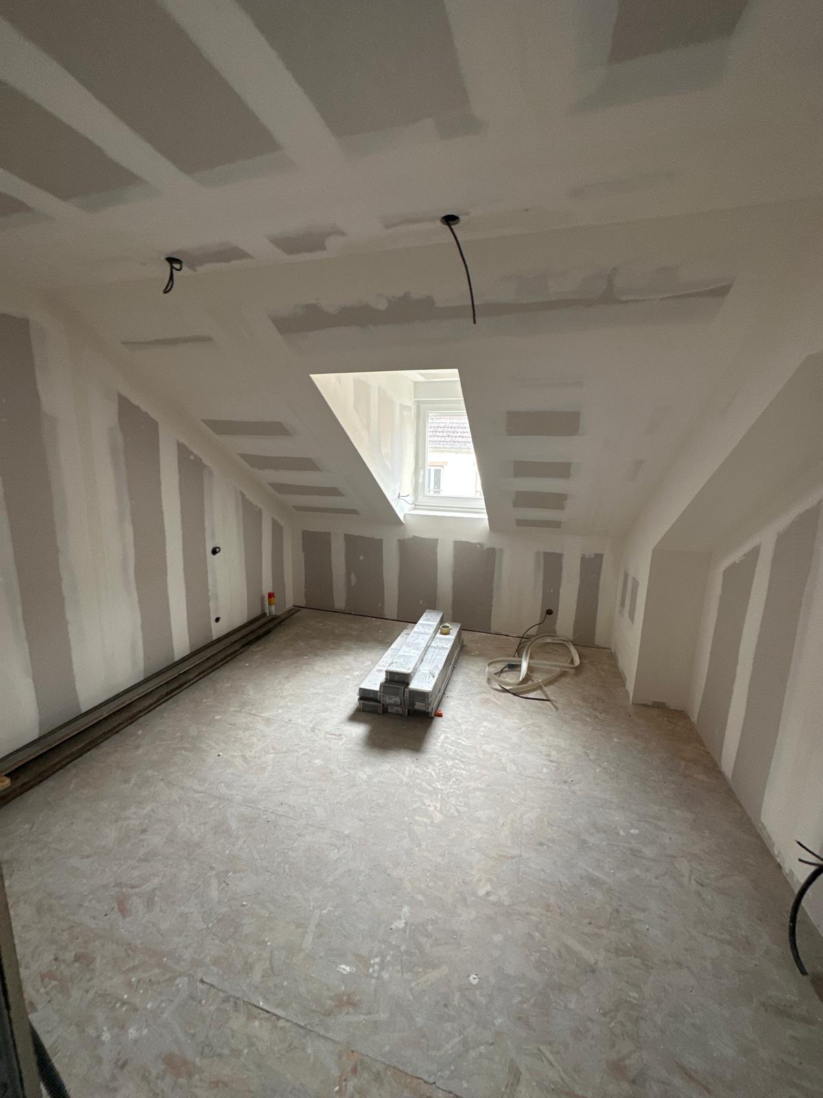 Combles en cours d’aménagement : plaques de plâtre jointées, fenêtre de toit posée, sol en OSB