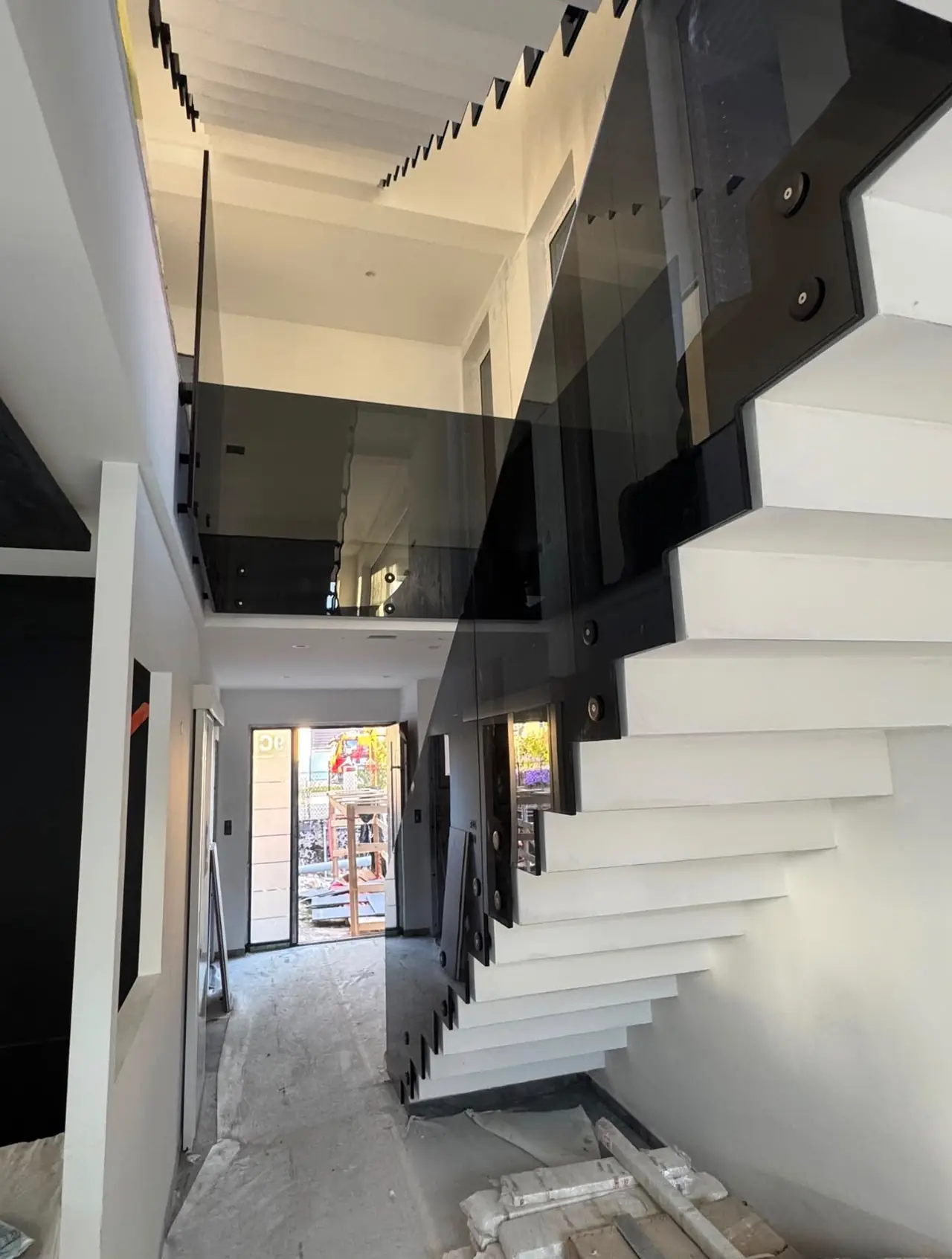 Escalier suspendu à marches blanches et garde-corps en verre fumé dans un volume à double hauteur ; sol encore protégé, finitions à faire