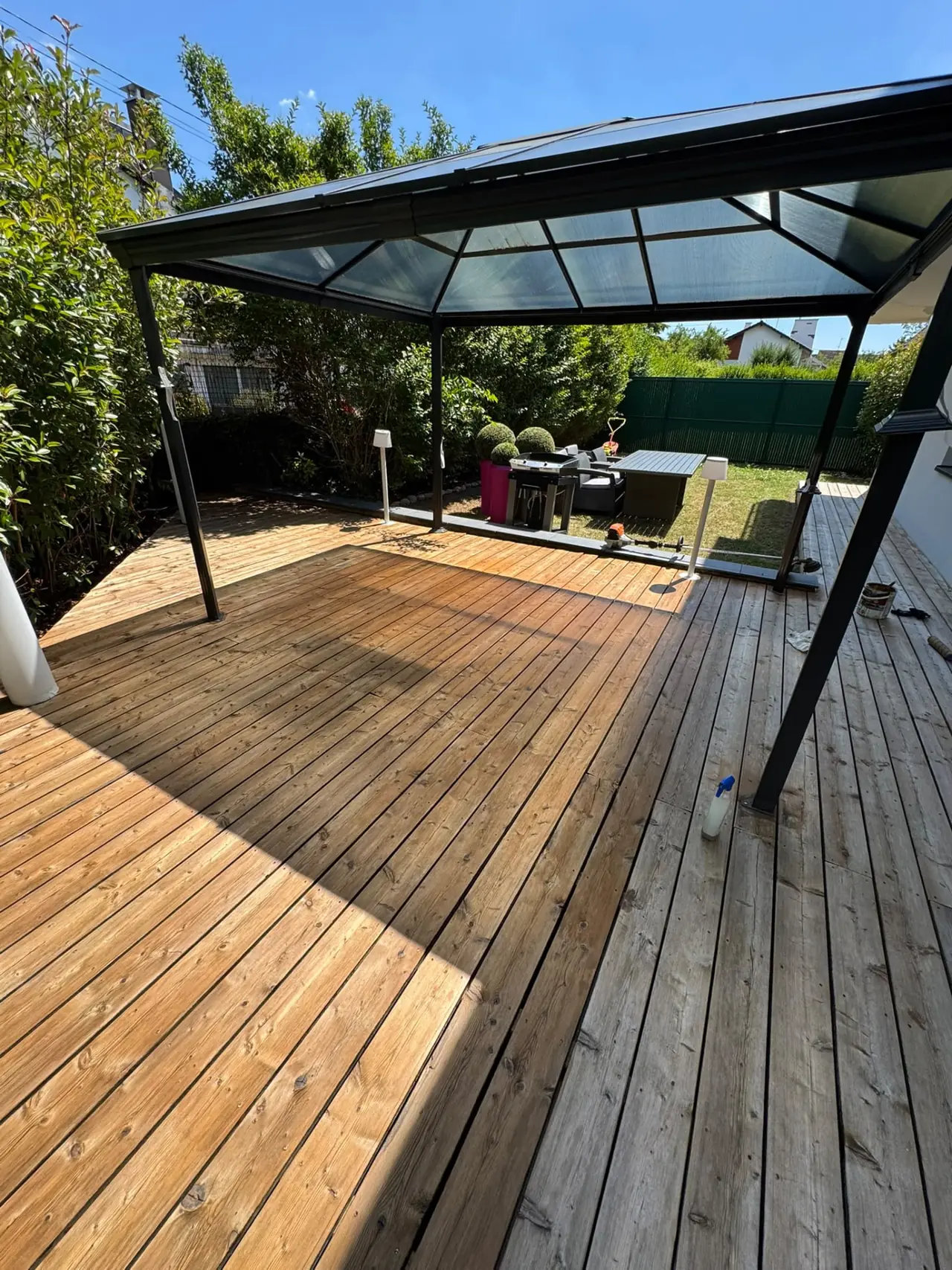 Terrasse en lames de bois sous une pergola à toit translucide, traitement du bois en cours