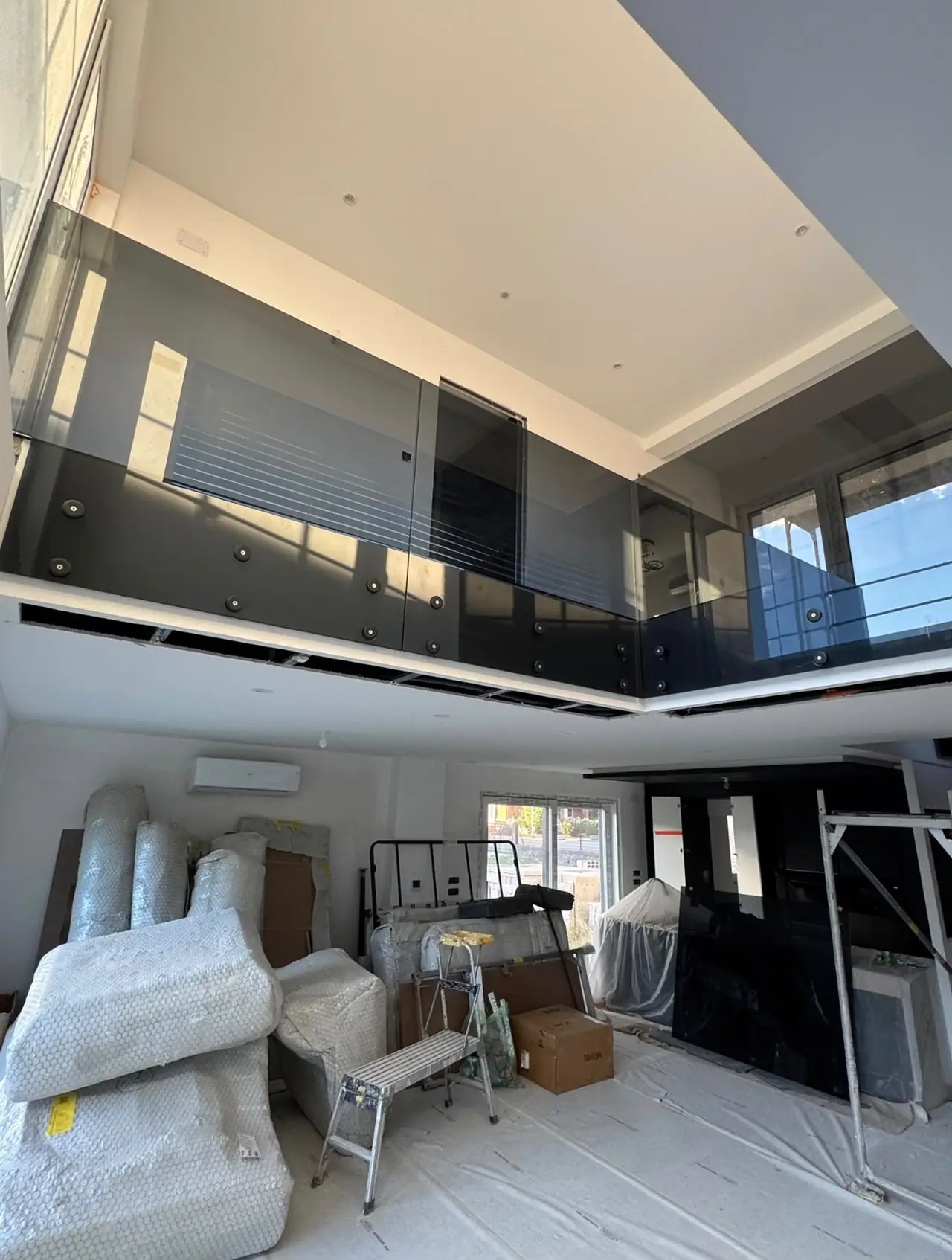Mezzanine à garde-corps en verre fumé au-dessus d’une pièce en travaux, meubles emballés et sol protégé