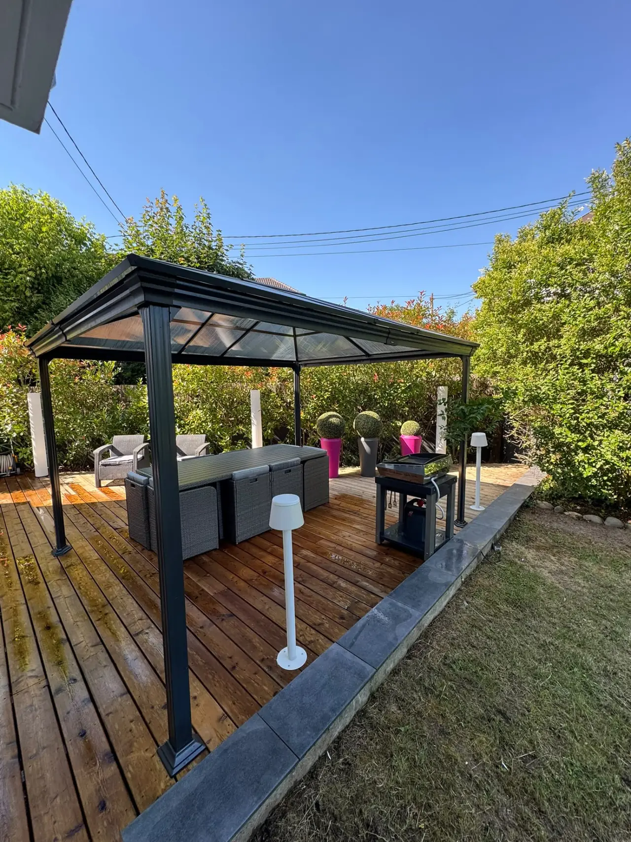 Terrasse en lames de bois avec pergola à toit translucide, salon de jardin et bordure grise