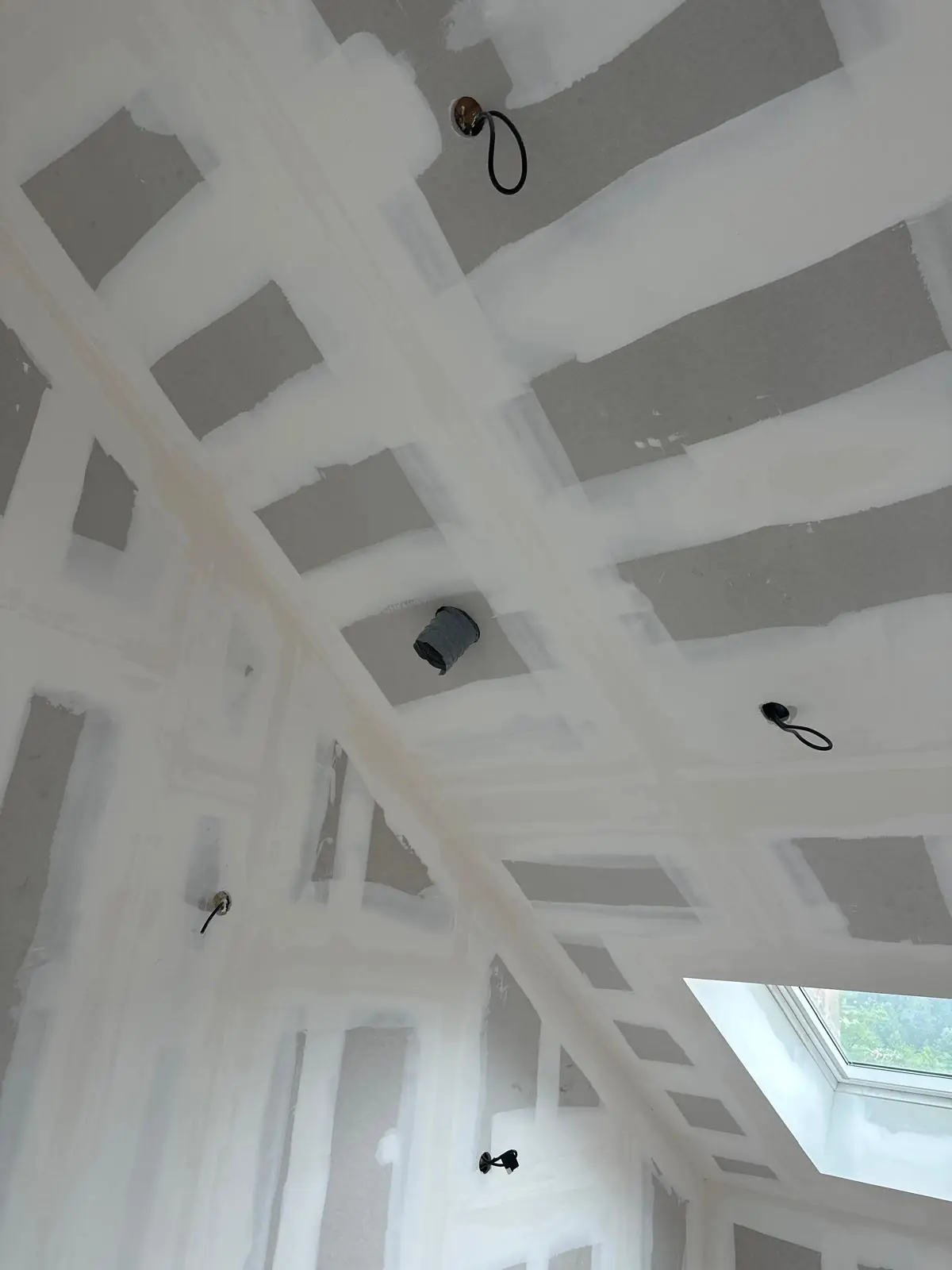 Plafond et rampants en plaques de plâtre aux joints enduits, autour d’une fenêtre de toit ; fils électriques en attente au plafond